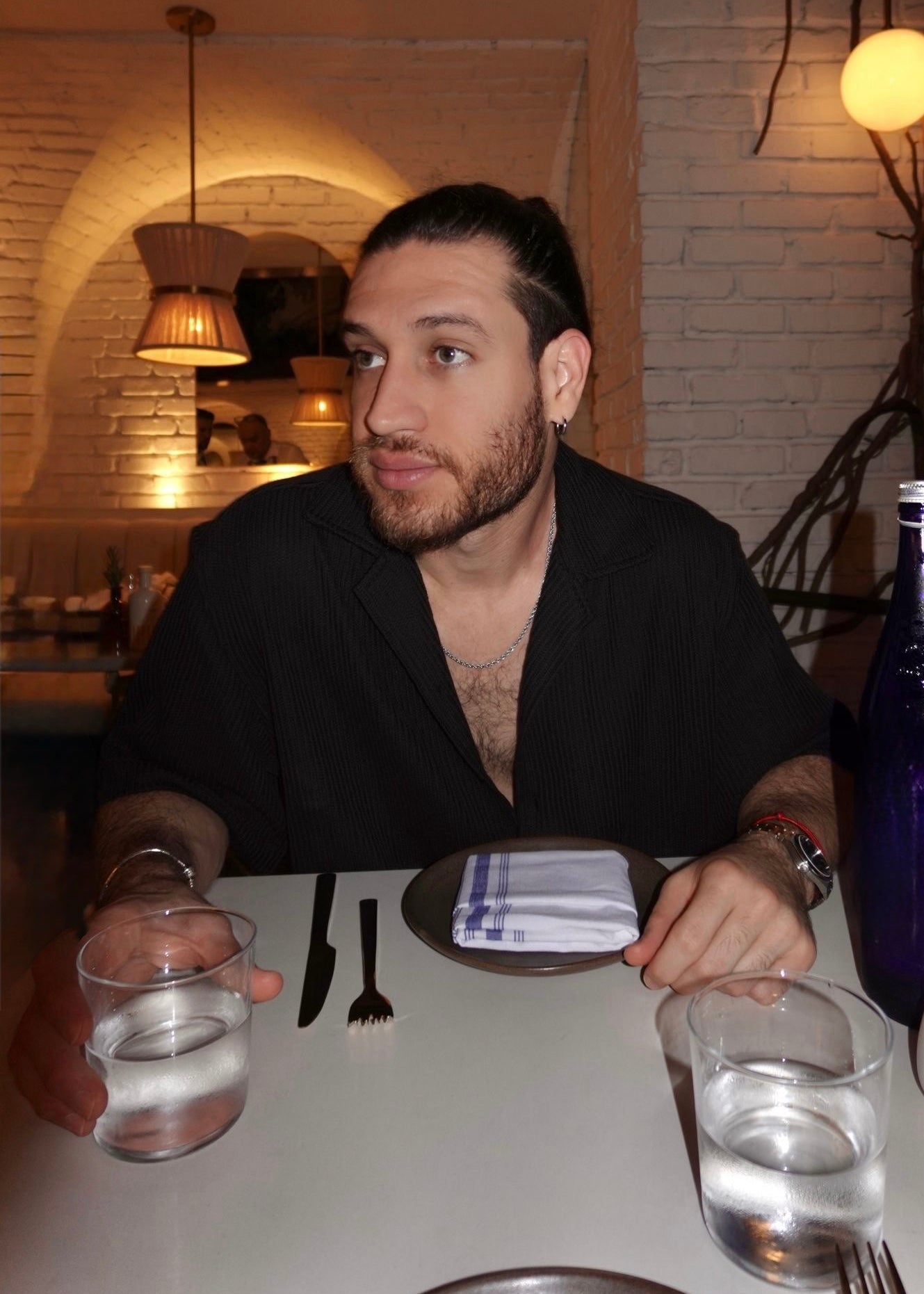 Man sitting at a table in a restaurant with summer outfit wearing jewelry